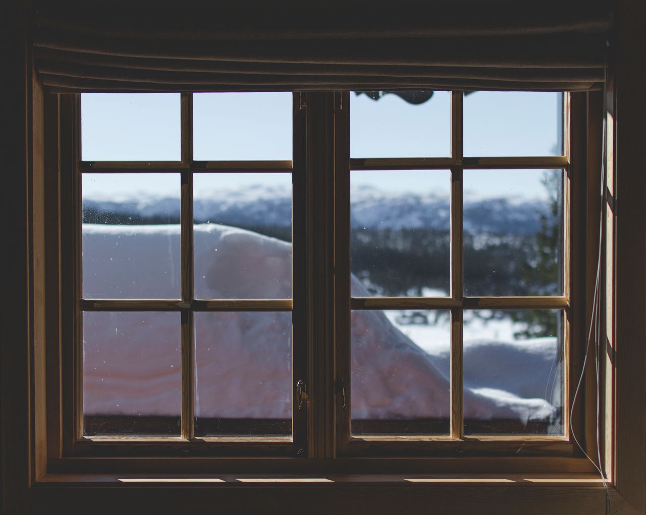 A scenic view of snow-capped mountains through a wooden window frame, capturing the serene winter landscape.